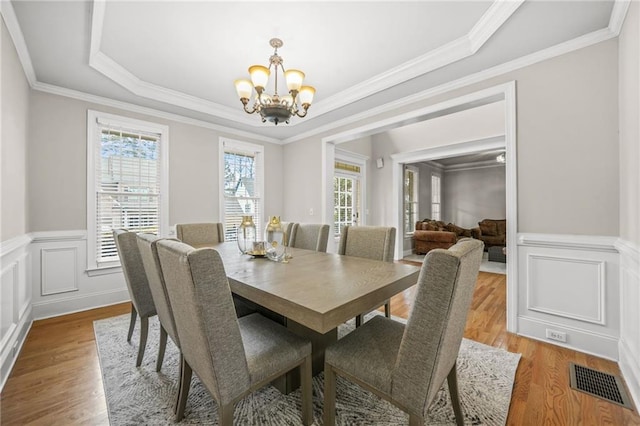 dining space with a wainscoted wall, visible vents, light wood-style floors, a decorative wall, and a notable chandelier