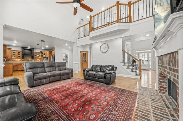 living room with light wood-style flooring, a ceiling fan, a fireplace, baseboards, and stairs