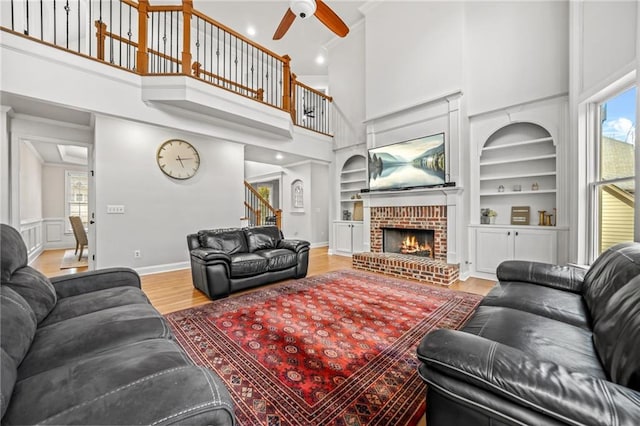 living room with stairway, built in features, wood finished floors, a fireplace, and ceiling fan