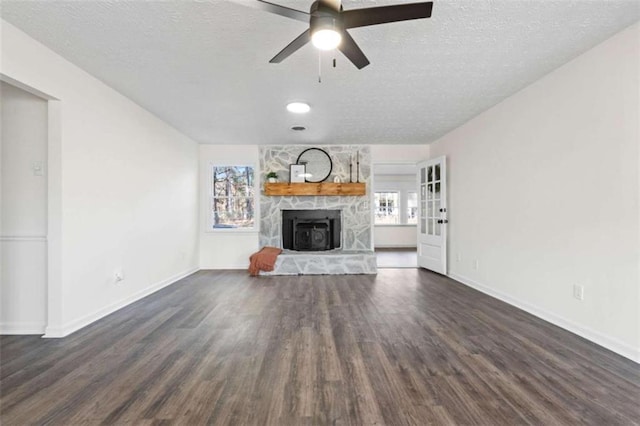 unfurnished living room featuring a stone fireplace, a textured ceiling, ceiling fan, and dark wood-type flooring