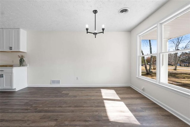 unfurnished dining area with a textured ceiling, a chandelier, a wealth of natural light, and dark wood-type flooring