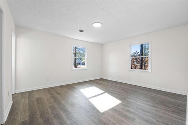 empty room with dark hardwood / wood-style flooring, a textured ceiling, and plenty of natural light