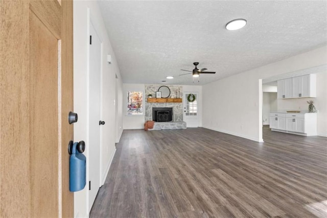 unfurnished living room featuring a fireplace, ceiling fan, a textured ceiling, and dark hardwood / wood-style floors