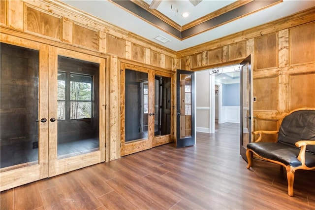 unfurnished room featuring dark wood-style floors, a tray ceiling, crown molding, french doors, and a decorative wall