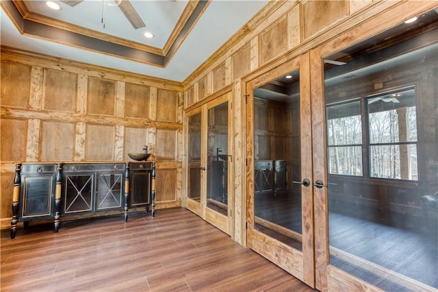 interior space featuring wooden walls, ornamental molding, a raised ceiling, and dark wood finished floors