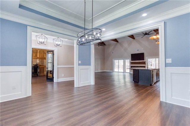 unfurnished dining area featuring a raised ceiling, a ceiling fan, dark wood finished floors, wainscoting, and crown molding