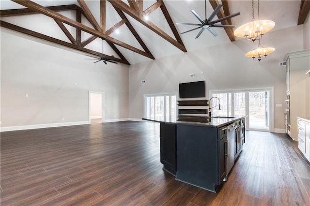 kitchen with decorative light fixtures, ceiling fan with notable chandelier, dark wood-style flooring, open floor plan, and a center island with sink