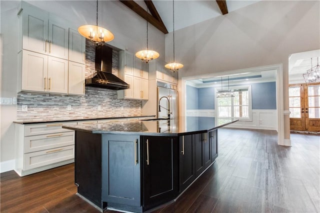 kitchen with pendant lighting, a center island with sink, dark wood-type flooring, white cabinets, and wall chimney exhaust hood