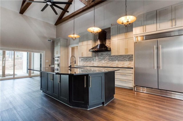 kitchen with wall chimney exhaust hood, a kitchen island with sink, stainless steel appliances, pendant lighting, and backsplash