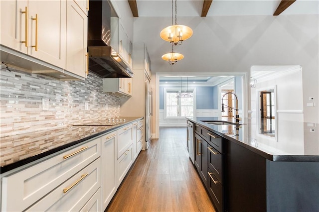 kitchen with wall chimney exhaust hood, dark countertops, a sink, and pendant lighting