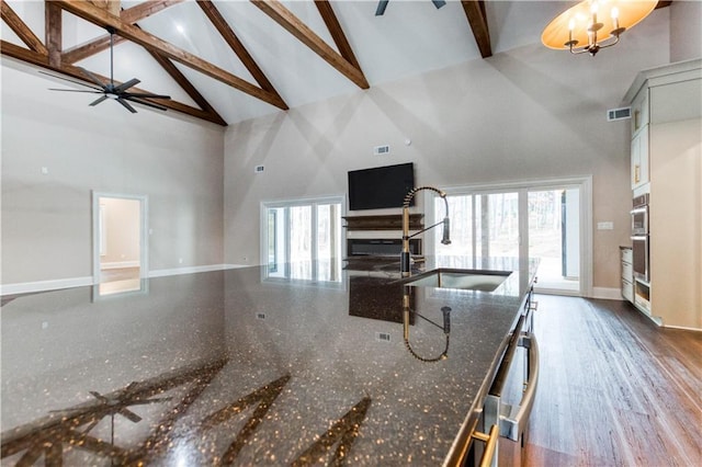 kitchen with visible vents, a ceiling fan, open floor plan, dark stone countertops, and a sink