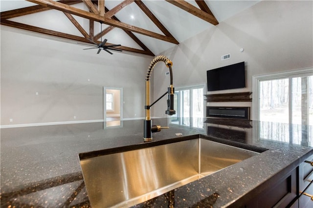 kitchen featuring a glass covered fireplace, open floor plan, a sink, dark stone countertops, and plenty of natural light