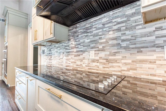 kitchen with dark wood-type flooring, dark stone counters, backsplash, and wall chimney range hood