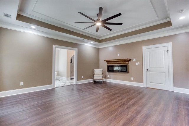 unfurnished room with wood finished floors, visible vents, ornamental molding, a raised ceiling, and a glass covered fireplace