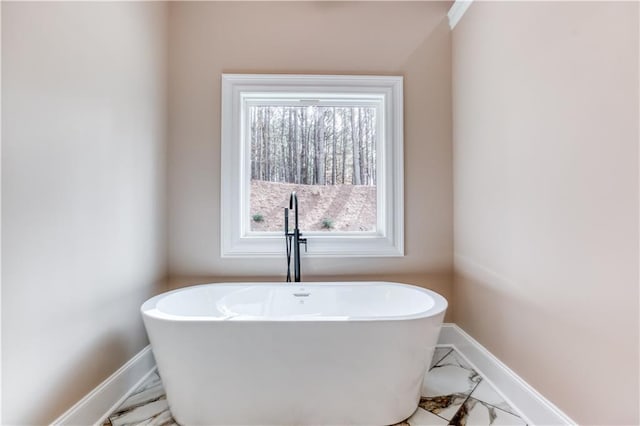 full bath with a freestanding tub, baseboards, and marble finish floor