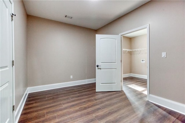 unfurnished bedroom featuring visible vents, baseboards, dark wood-style flooring, a spacious closet, and a closet