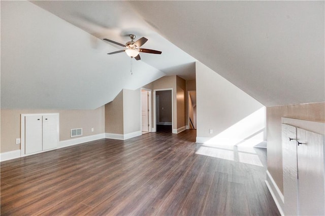 additional living space featuring dark wood finished floors, visible vents, a ceiling fan, vaulted ceiling, and baseboards