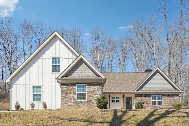 view of front of house with stone siding, roof with shingles, board and batten siding, and a front lawn