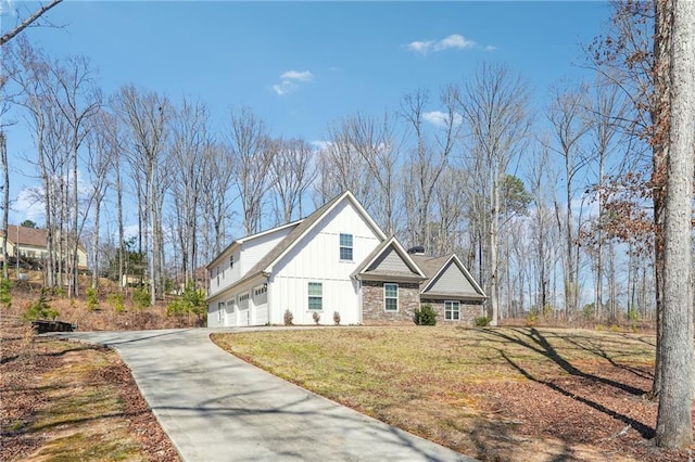 view of side of property featuring driveway, an attached garage, stone siding, a lawn, and board and batten siding