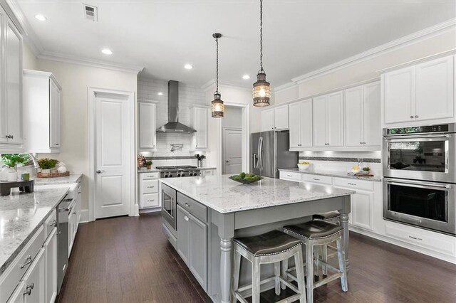 kitchen with stainless steel appliances, wall chimney range hood, a kitchen island, a breakfast bar area, and white cabinets