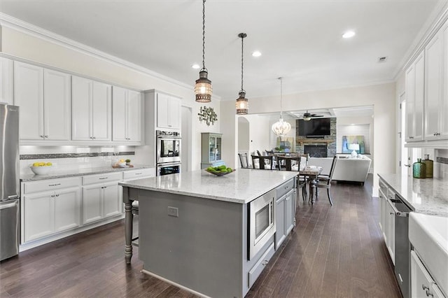 kitchen featuring light stone countertops, pendant lighting, white cabinets, appliances with stainless steel finishes, and a fireplace