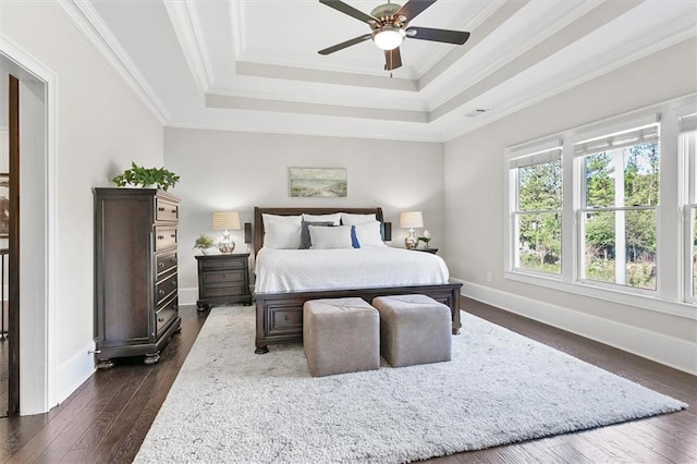 bedroom featuring dark wood-type flooring, a raised ceiling, ceiling fan, and ornamental molding