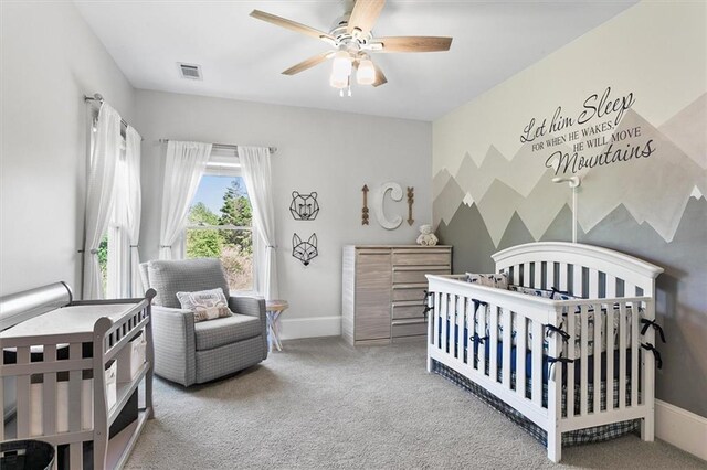 carpeted bedroom featuring a nursery area and ceiling fan