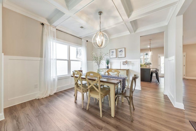 dining space with hardwood / wood-style flooring, beamed ceiling, an inviting chandelier, crown molding, and coffered ceiling