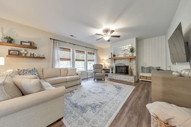 living room with dark wood-type flooring, a stone fireplace, and ceiling fan