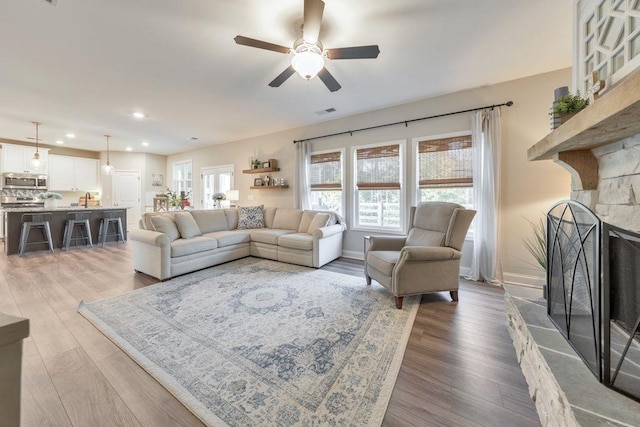 living room with ceiling fan, hardwood / wood-style flooring, and a stone fireplace