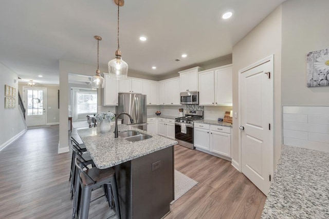 kitchen with light stone counters, white cabinetry, appliances with stainless steel finishes, pendant lighting, and hardwood / wood-style flooring