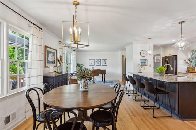 dining space featuring ornamental molding, sink, a notable chandelier, and light wood-type flooring