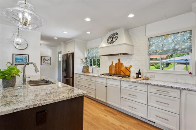 kitchen with pendant lighting, sink, premium range hood, appliances with stainless steel finishes, and white cabinets