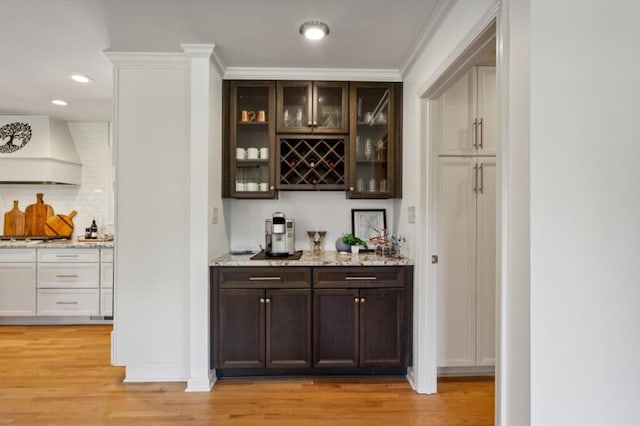 bar with dark brown cabinetry, light hardwood / wood-style flooring, light stone countertops, and premium range hood