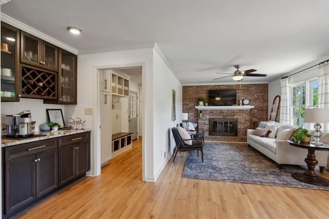 living room featuring crown molding, a fireplace, light hardwood / wood-style floors, and ceiling fan