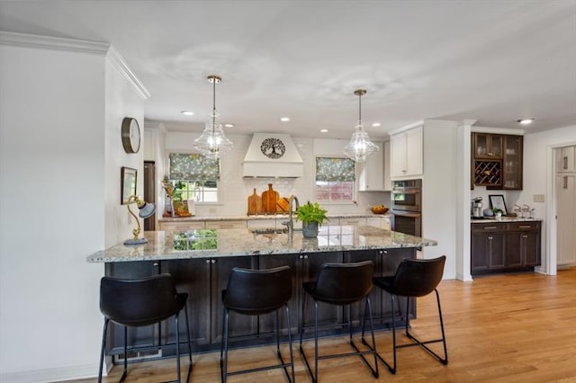 kitchen featuring white cabinetry, a breakfast bar area, dark brown cabinetry, custom range hood, and stainless steel double oven