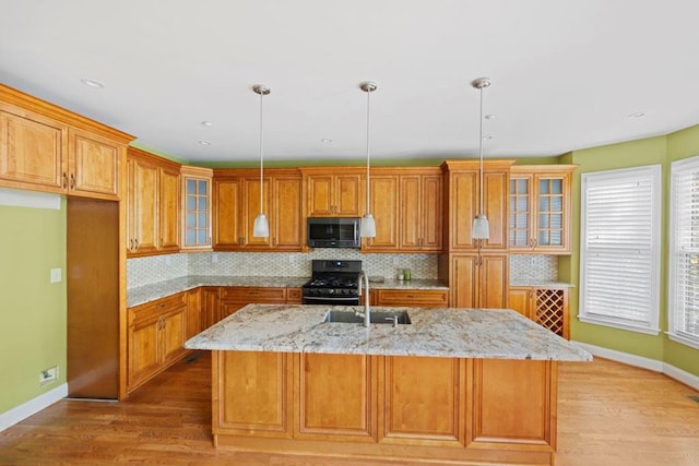 kitchen with tasteful backsplash, light stone counters, light hardwood / wood-style floors, decorative light fixtures, and a center island with sink