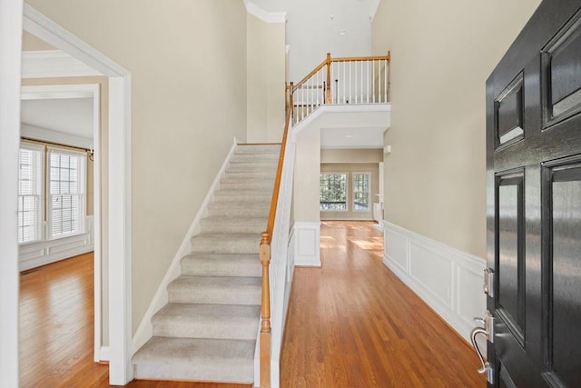 entryway with a towering ceiling, ornamental molding, and light wood-type flooring