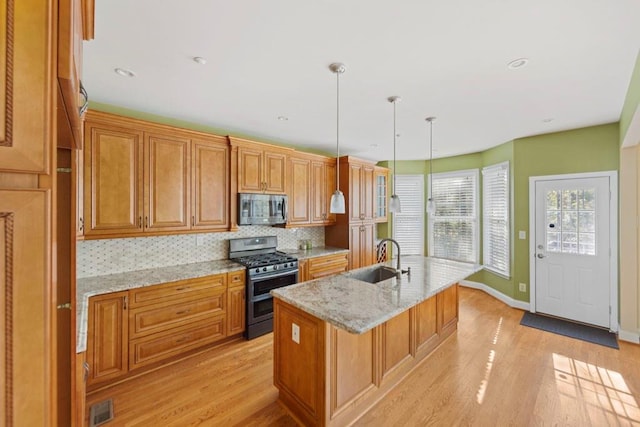 kitchen featuring appliances with stainless steel finishes, light wood-type flooring, a kitchen island with sink, sink, and pendant lighting