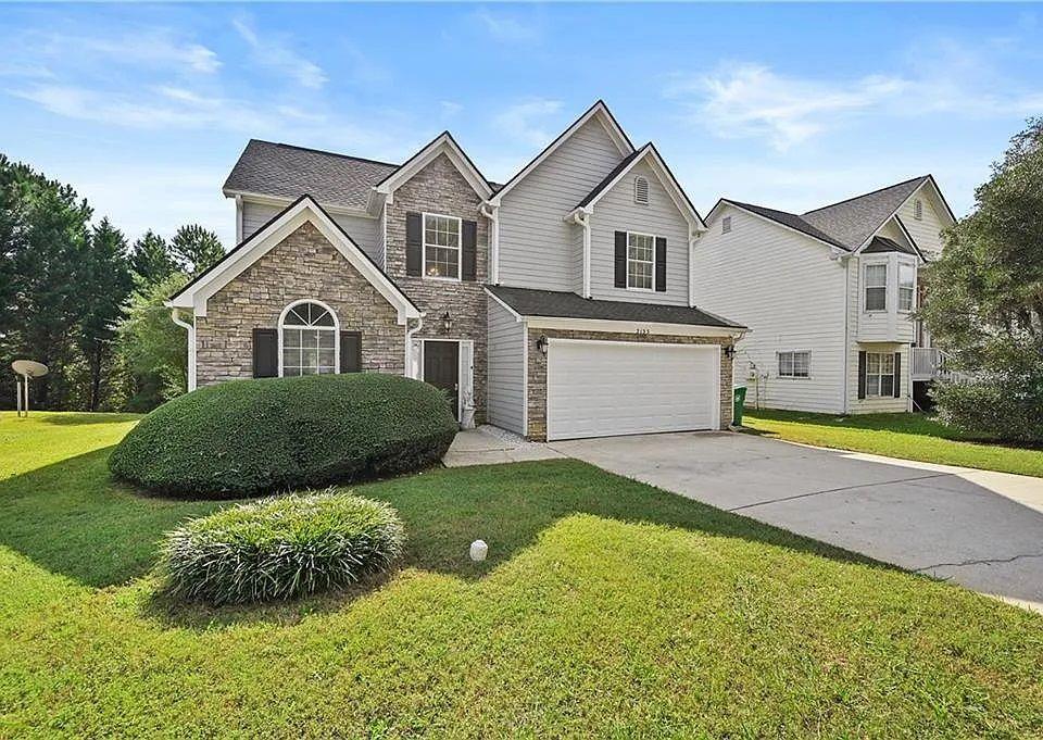 traditional home with an attached garage, stone siding, concrete driveway, and a front yard