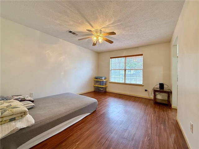 bedroom with ceiling fan, dark hardwood / wood-style flooring, and a textured ceiling