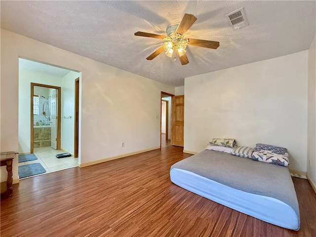 bedroom featuring ceiling fan, ensuite bath, a textured ceiling, and light wood-type flooring