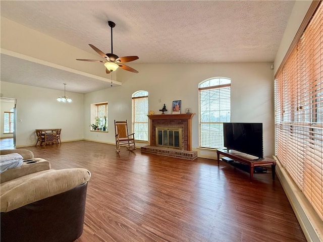 living room featuring vaulted ceiling, dark hardwood / wood-style floors, ceiling fan with notable chandelier, a fireplace, and a textured ceiling