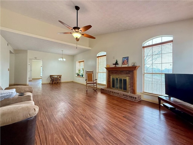 living room featuring ceiling fan with notable chandelier, a fireplace, lofted ceiling, dark wood-type flooring, and a textured ceiling