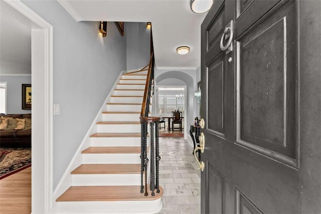 foyer entrance with ornamental molding, arched walkways, baseboards, and stairs