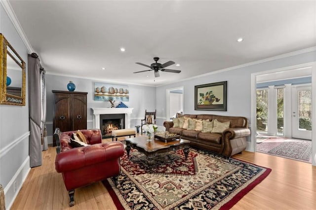 living room with crown molding, recessed lighting, light wood-style flooring, ceiling fan, and a warm lit fireplace