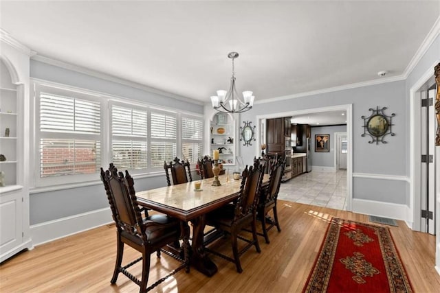 dining area with light wood-type flooring, crown molding, baseboards, and an inviting chandelier