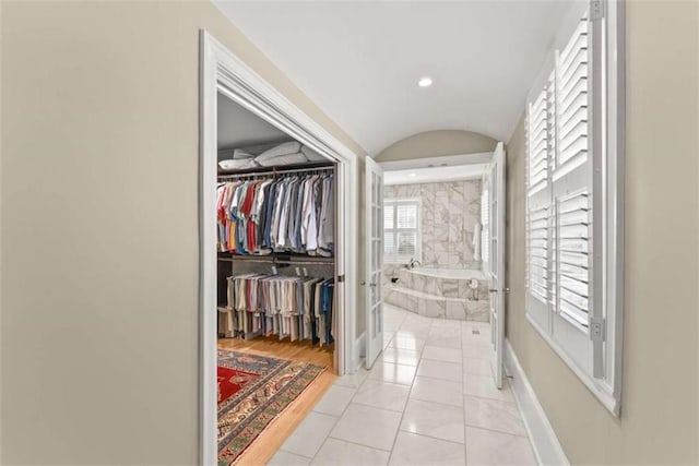 hallway featuring lofted ceiling, baseboards, recessed lighting, and light tile patterned floors