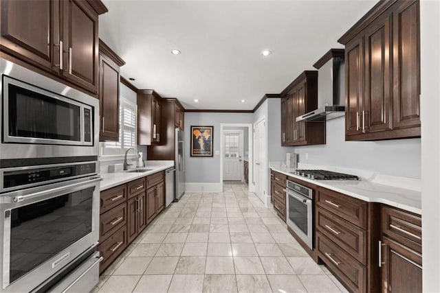 kitchen with appliances with stainless steel finishes, marble finish floor, crown molding, wall chimney range hood, and a sink