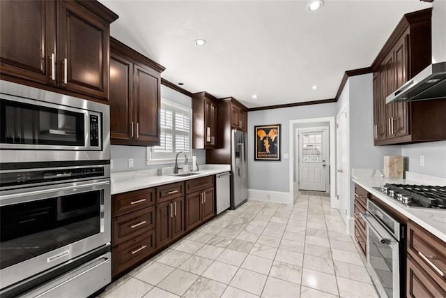 kitchen with appliances with stainless steel finishes, crown molding, wall chimney range hood, a sink, and a warming drawer